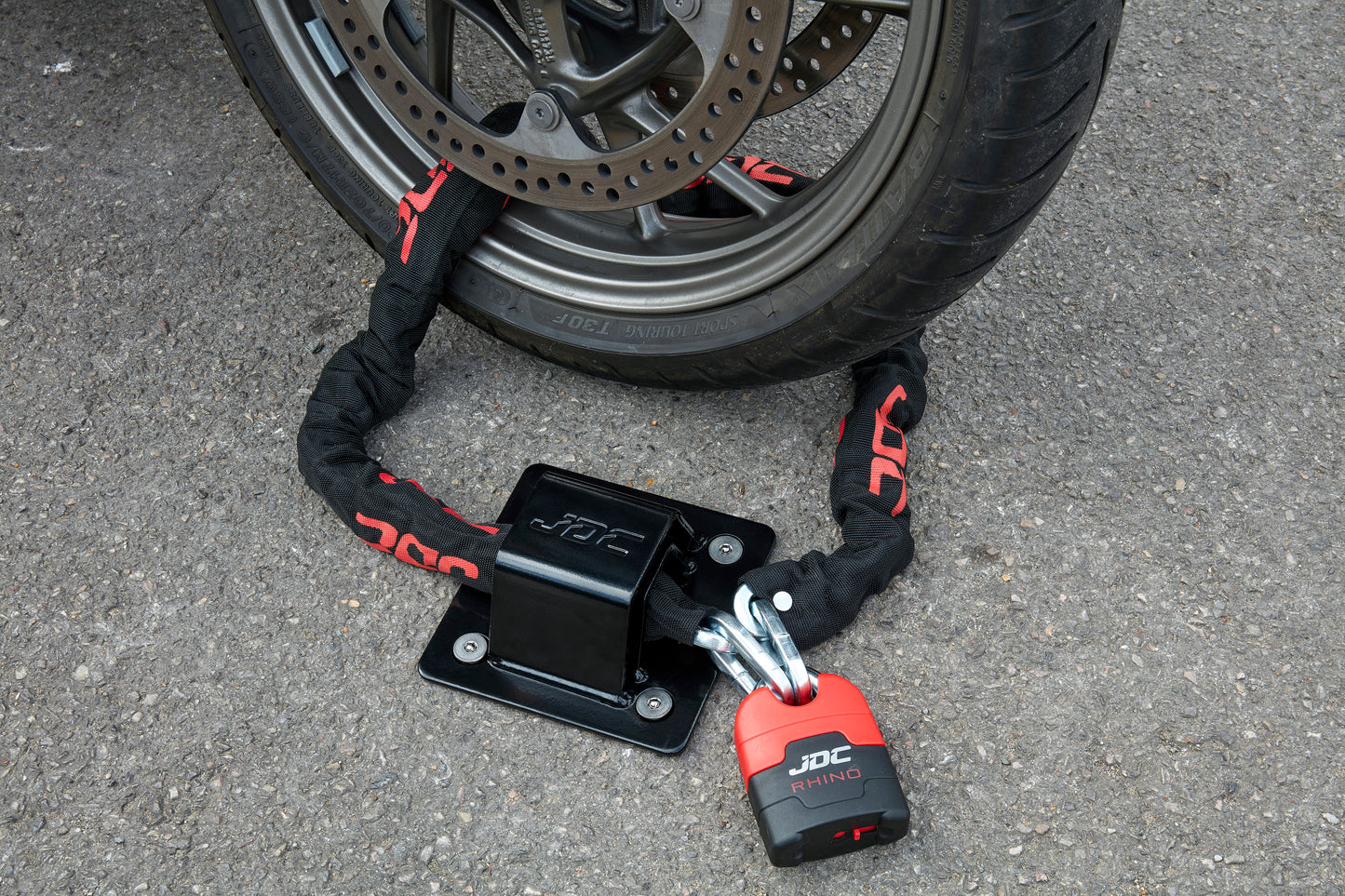 JDC Product's Sphere Ground Anchor Pro (black) shown with JDC Heavy Duty Bike Chain securing a motorcycle